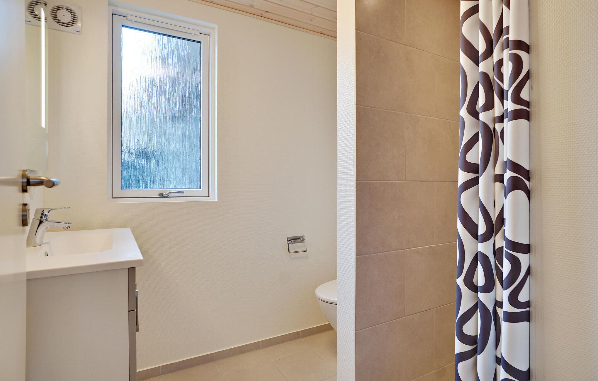 Un baño con ventana, lavamanos, inodoro y cortina de ducha.