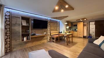 Ein gemütliches Wohnzimmer mit einem Flachbildfernseher, Holzdekor, einem Esstisch mit Stühlen und einem Sofa.