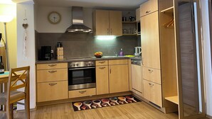 Una cucina compatta con mobili in legno, un fornello e un forno a microonde. Sul muro c'è un orologio e un addobbo appeso.