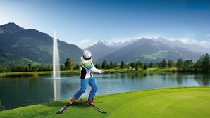 Una persona scia su una pista verde, con un lago e montagne sullo sfondo.
