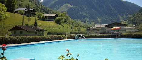 A swimming pool with a mountain backdrop, surrounded by potted plants and a few buildings.