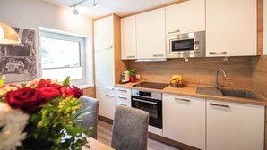 Una cucina moderna con mobili bianchi, un forno a microonde in acciaio inossidabile e un lavello. Si vede una finestra con vista su spazi verdi.