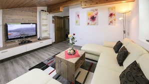 Un soggiorno con televisore a schermo piatto, un tavolino in legno, un divano color beige e un vaso rosso con fiori.
