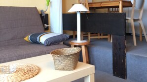 Een woonkamer met een bank, een tafel met een lamp, een eettafel met stoelen en een keuken met kasten.
