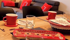 Une table à manger avec des tasses rouges, un verre, des couverts et un plateau orné de motifs en forme de cœur.