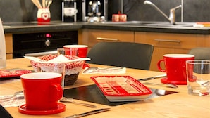 Un coin cuisine avec une table à manger dressée pour quatre personnes, comprenant des tasses et un mug rouges, une machine à café et un four à micro-ondes.