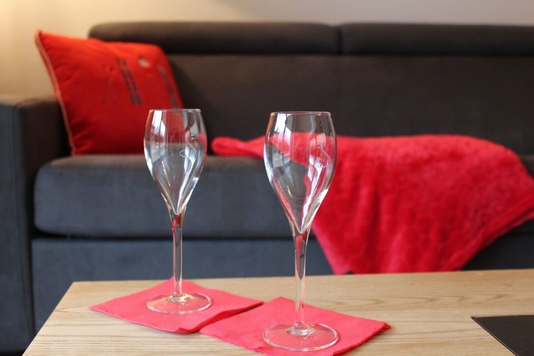 Two empty wine glasses on a wooden table with a red napkin, placed in front of a dark grey sofa with a red pillow.