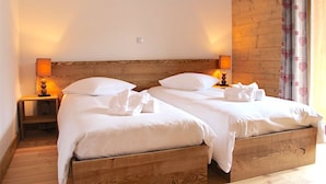 Un lit double avec une tête de lit et un pied de lit en bois, deux tables de chevet avec des lampes et une fenêtre agrémentée de rideaux à motifs floraux.