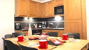 Une cuisine avec des meubles de rangement en bois, un four à micro-ondes et une table à manger dressée avec des tasses et des assiettes rouges.