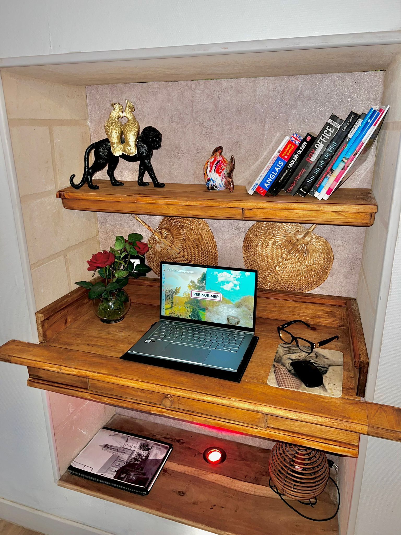 A wooden shelf unit with decorative items, books, a laptop, and a vase with a red rose.