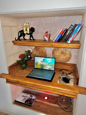 A wooden shelf unit with decorative items, books, a laptop, and a vase with a red rose.