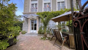 A courtyard with a brick pathway, outdoor seating, and a building with a balcony. - Large, Comfortable, Air-Conditioned Historic House with a Sauna. (Ver-sur-Mer)
