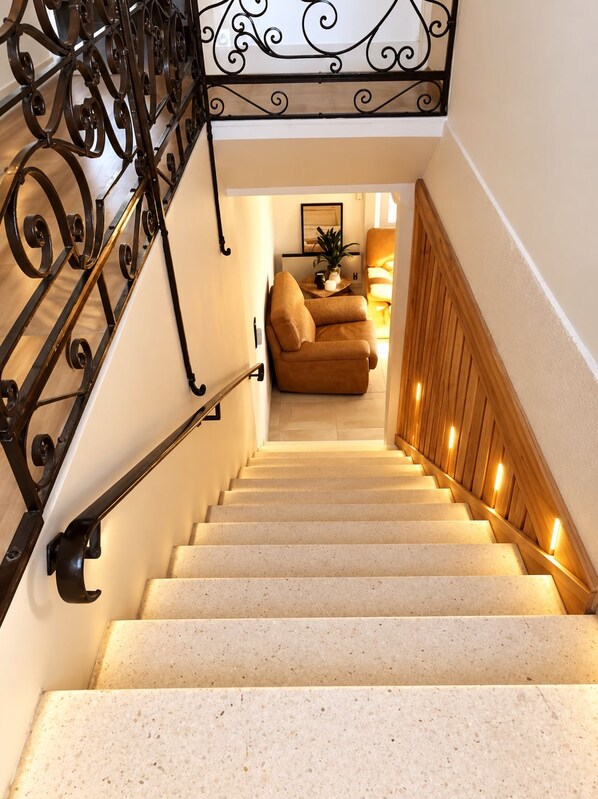 A staircase with a wrought iron railing, leading to a living area with a sofa and a table.