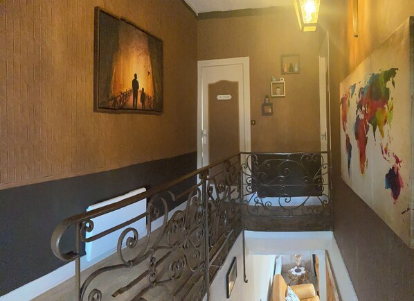 A hallway with a wooden wall, a metal railing, a door, and a colorful abstract painting. - Large, Comfortable, Air-Conditioned Historic House with a Sauna. (Ver-sur-Mer)