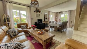 A spacious living room with a leather sofa, a wooden coffee table, and a dining area with a table set for four. - Large, Comfortable, Air-Conditioned Historic House with a Sauna. (Ver-sur-Mer)