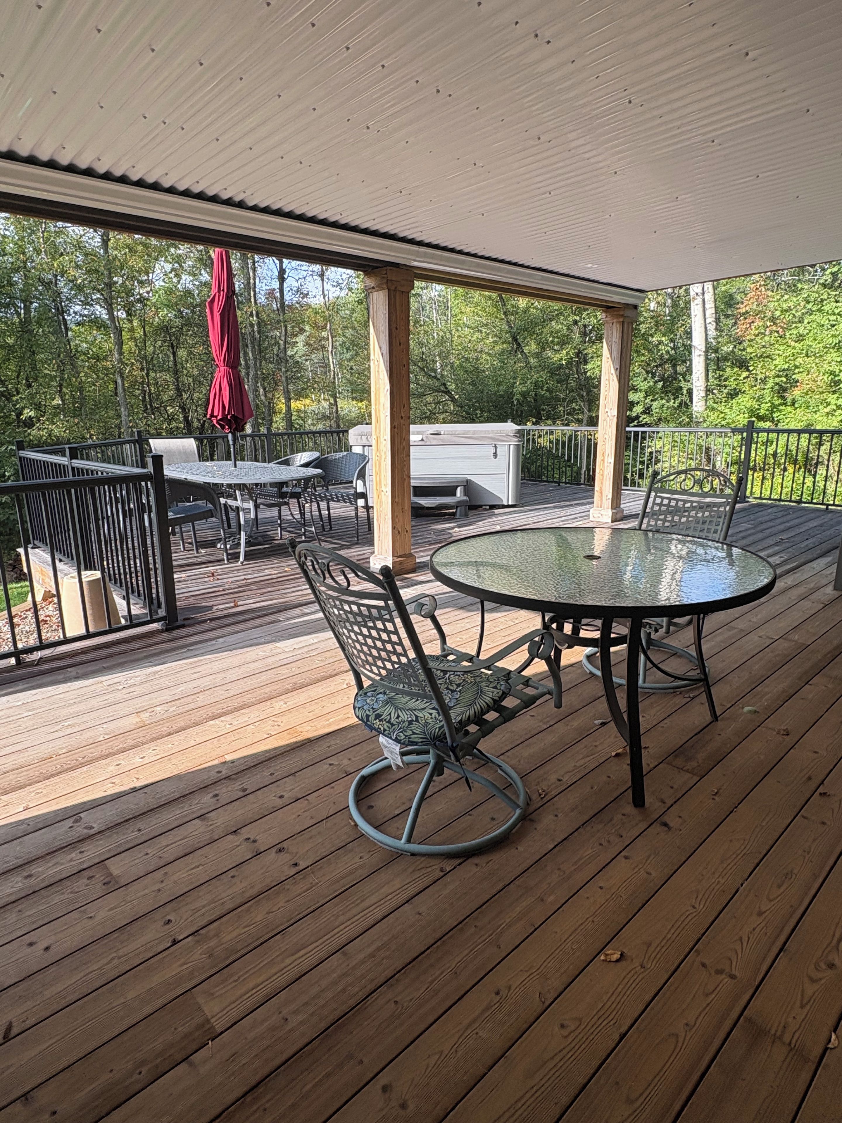 A wooden deck with a glass-top table and chairs, a hot tub, and a red umbrella.