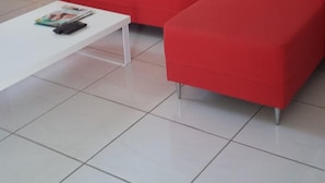 Un sofá seccional rojo, una mesa de centro blanca y un jarrón grande sobre un piso de baldosas.