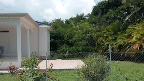 Un espacio cubierto de césped con un edificio blanco, posiblemente un hotel, y abundante vegetación al fondo.