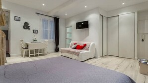 Een moderne slaapkamer met een bed, een bureau, een stoel, een bank met een rood kussen, een televisie en een garderobe.
