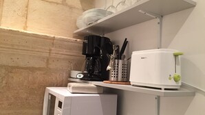 Een compacte keuken met een magnetron, koffiezetapparaat, broodrooster en planken met borden en glazen.
