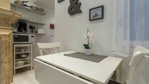 Een compacte keuken met een wit aanrecht, een magnetron, en een klein zitehoekje met een witte stoel en een potorkidee.
