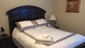 A neatly made bed with white linens and a folded towel, a bedside lamp, and a framed picture on the wall. - Charming Singingwood House (Sacramento)