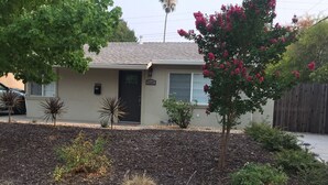 A residential house with a front yard featuring a small tree, a rock garden, and a driveway. - Charming Singingwood House (Sacramento)