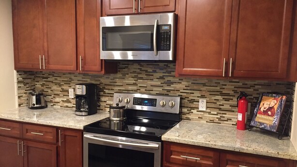 A kitchen with stainless steel appliances, wooden cabinets, a tiled backsplash, and a granite countertop. - Charming Singingwood House (Sacramento)