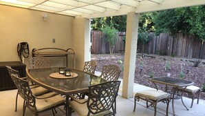 An outdoor patio with a glass-top table and chairs, surrounded by a wooden fence and garden beds. - Charming Singingwood House (Sacramento)