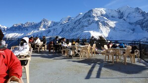 Eine Terrasse mit Tischen und Stühlen mit Blick auf ein verschneites Gebirge.
