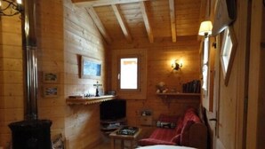 Ein gemütliches Holzhaus-Interieur mit Kamin, Fernseher und einem roten Sofa.