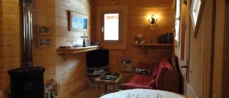 Interno accogliente di una baita di legno con camino, televisore e un divano rosso.
