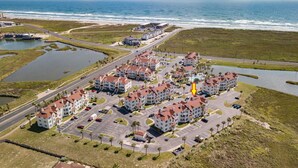 Vue aérienne d’un hôtel situé sur la côte, composé de plusieurs bâtiments, de parkings et d’un port de plaisance.