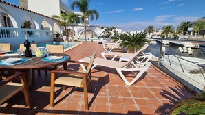 Un área junto a la piscina con sillones de descanso, una mesa de comedor con platos, vasos y una botella.