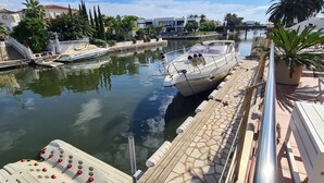 Puerto deportivo con barcos amarrados, un camino de piedra y una zona de restaurante con mesas al aire libre.