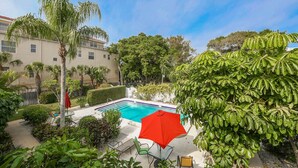 A swimming pool surrounded by lush greenery, with a red umbrella and outdoor furniture. - The Little Sandy...#1 in Siesta! (Siesta Key)