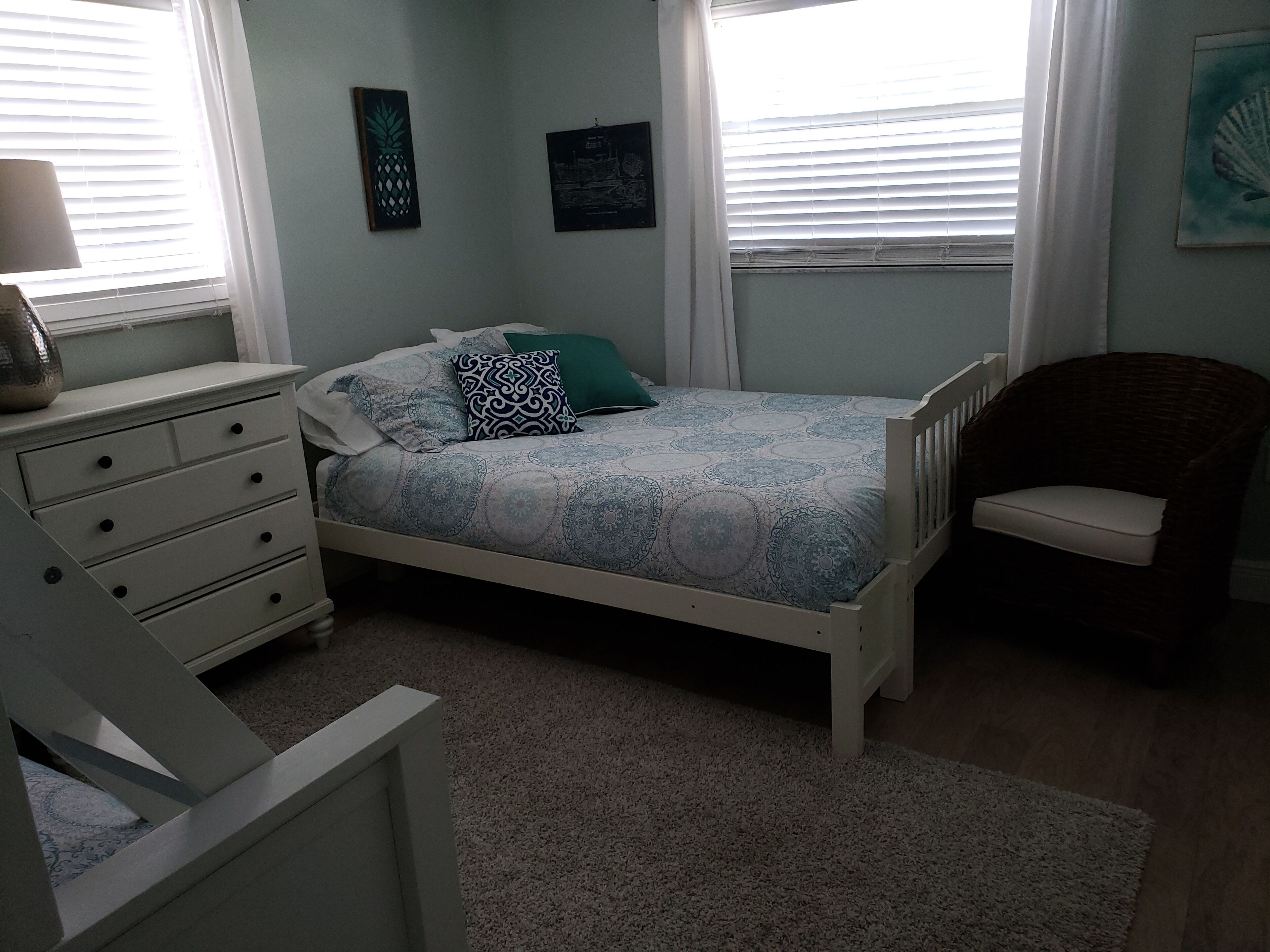 A bedroom with a bed, a dresser, a chair, and two wall art pieces.