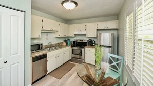 A compact kitchen with white cabinets, stainless steel appliances, and a glass dining table. - The Little Sandy...#1 in Siesta! (Siesta Key)