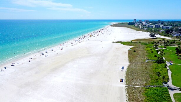 An aerial view of a beach with a long stretch of white sand, a clear blue ocean, and a few buildings in the background. - The Little Sandy...#1 in Siesta! (Siesta Key)