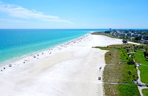 An aerial view of a beach with a long stretch of white sand, a clear blue ocean, and a few buildings in the background. - The Little Sandy...#1 in Siesta! (Siesta Key)