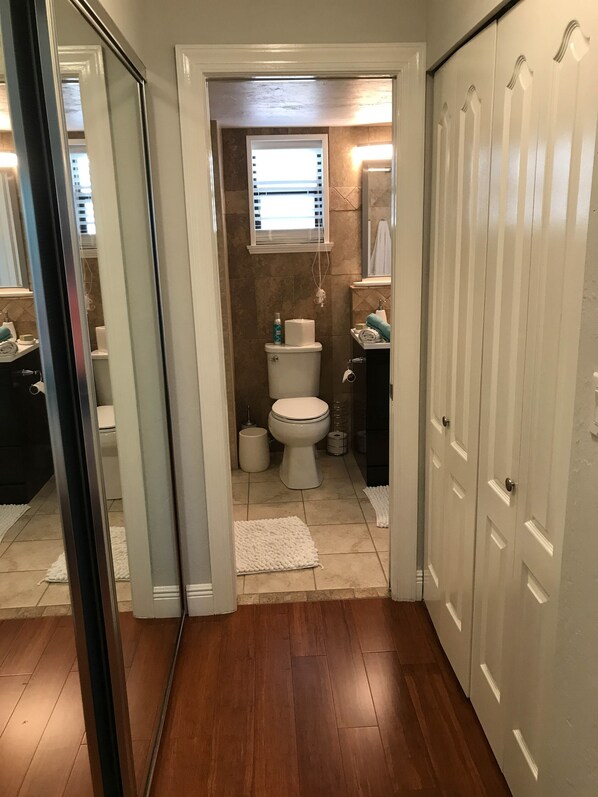 Un baño con inodoro, bidé y barra para toallas. Hay una ventana con persianas, un espejo y una toalla en el suelo.