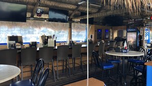 Un restaurante con techo de paja, zona de bar y disposición de mesas.