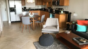 Una cocina moderna con armarios de madera, un refrigerador de acero inoxidable y un microondas. Hay un comedor con una mesa redonda y sillas, y una sala de estar con un sofá y una mesa de centro.