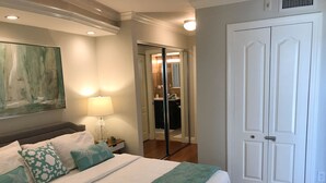 Una cama bien hecha con una colcha a rayas, una lámpara de noche y almohadones decorativos. Un cuadro abstracto de gran tamaño adorna la pared sobre la cama.