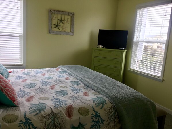 A bedroom with a bed, a dresser, a television on top, and a wall clock.
