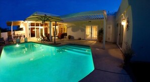 Une piscine avec un espace patio, des sièges extérieurs et une partie abritée.