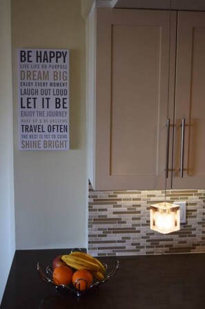 Une cuisine avec une citation inspirante sur le mur, un panier de fruits sur le plan de travail et un luminaire moderne.