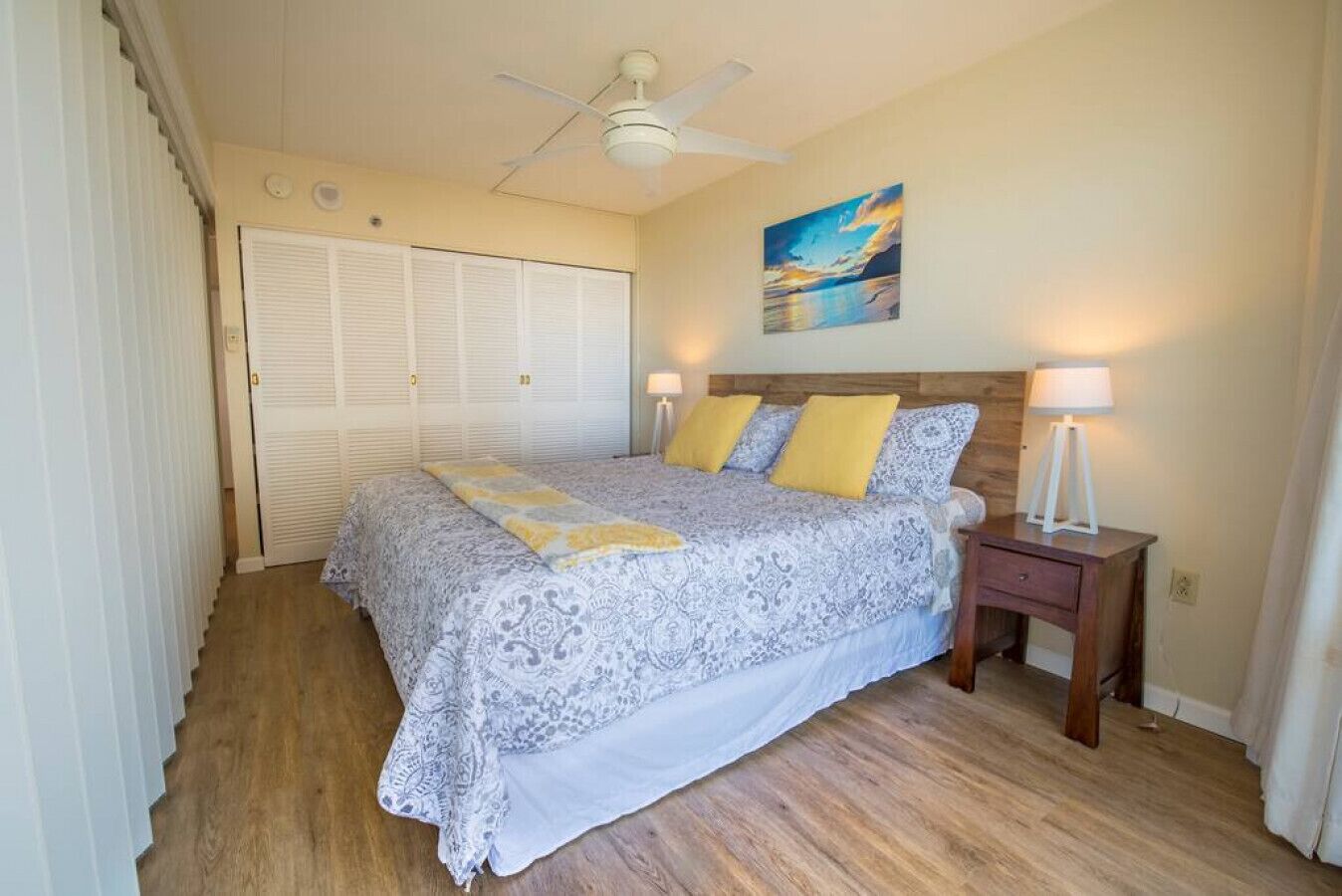 A bedroom with a bed, bedside lamps, a ceiling fan, and a painting on the wall.
