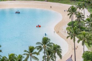 Une plage avec une eau d’un bleu limpide, des palmiers et des gens qui profitent des lieux.