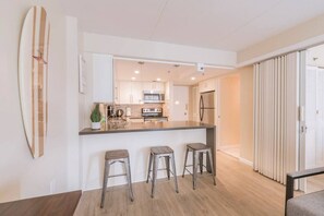 A modern kitchen with a central island, three bar stools, and a surfboard on the wall.